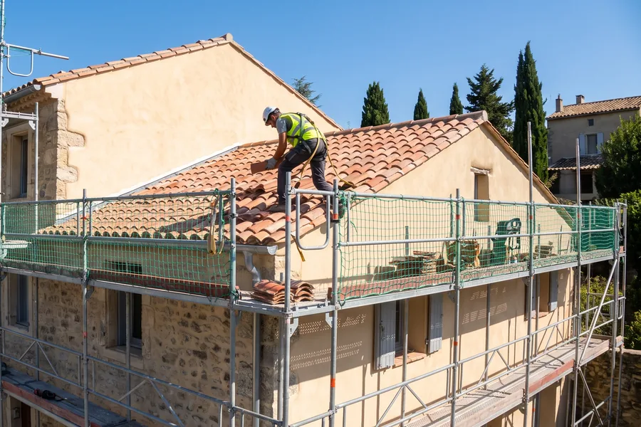 Couvreur sur échafaudage lors d'une rénovation de toiture en tuile canal dans l'Aude
